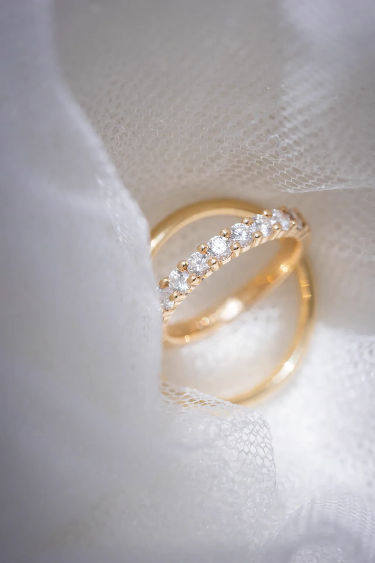 Alliances en or et diamants posées sur un voile de mariée